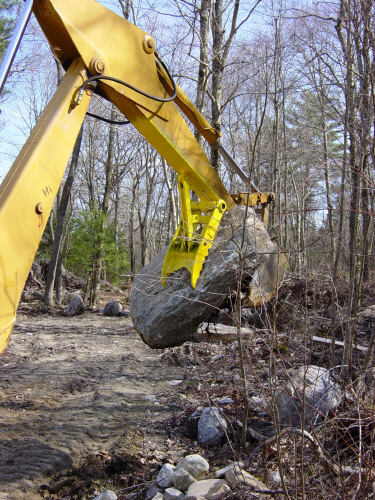 The MT1230 thumb, installed on an excavator, lifts a large stone.