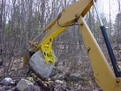 The MT1230 excavator thumb, installed on an excavator, lifts a very heavy stone.