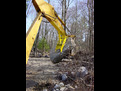 The MT1230 thumb, installed on an excavator, lifts a large stone.