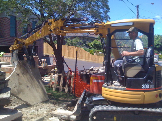 CAT 303 SR mini excavator picks up a large slab of concrete with 8"x30" thumb